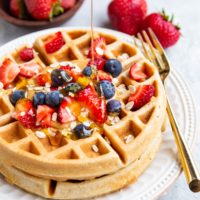 Honey being poured on top of waffles with fresh berries and almond butter.