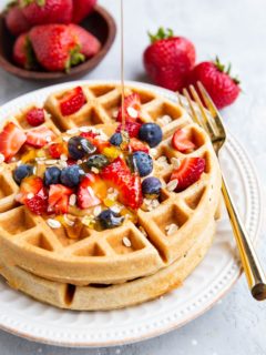 Honey being poured on top of waffles with fresh berries and almond butter.