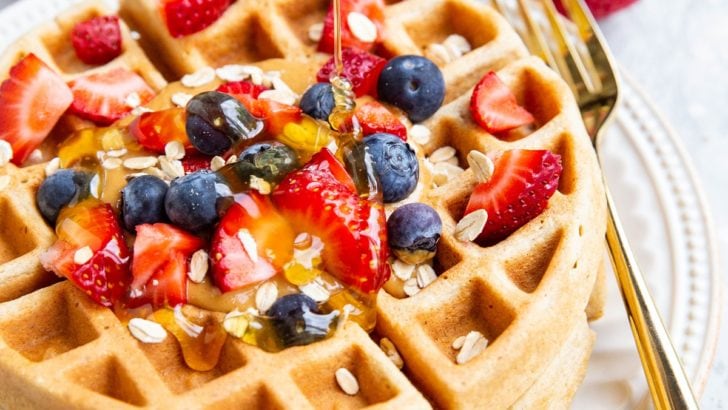 Honey being poured on top of waffles with fresh berries and almond butter.