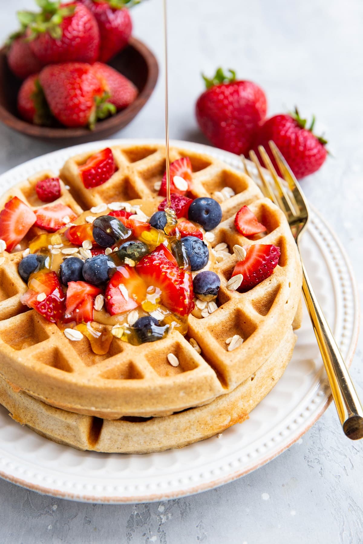 Honey being poured on top of waffles with fresh berries and almond butter.