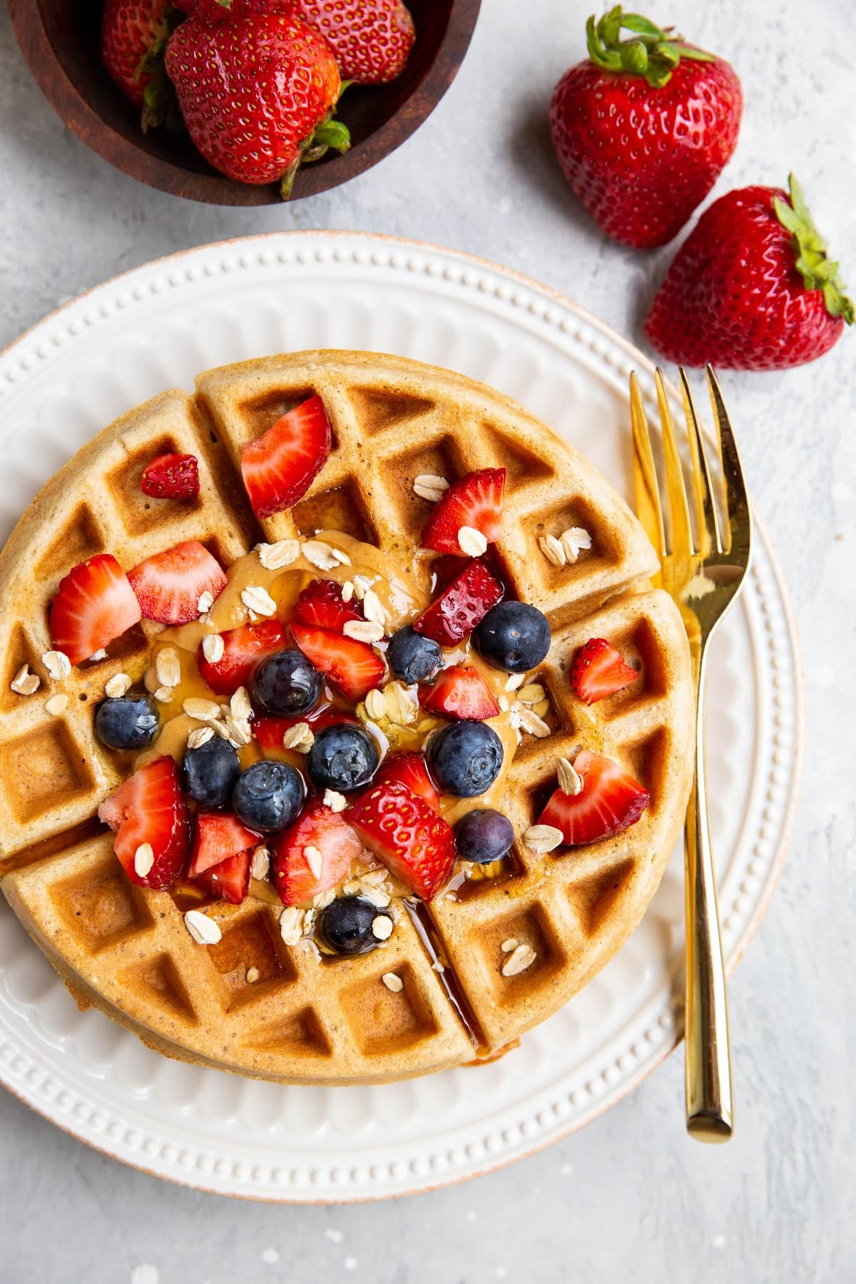 Large waffle on a plate with fresh strawberries and blueberries and a gold fork.