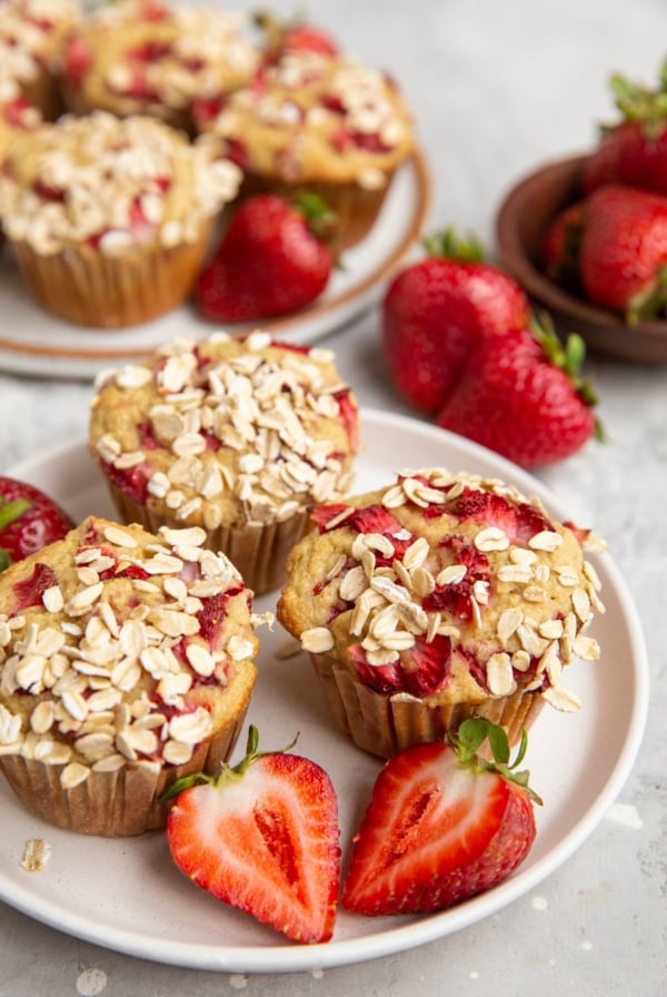 White plate of oatmeal strawberry muffins and fresh strawberries all around.