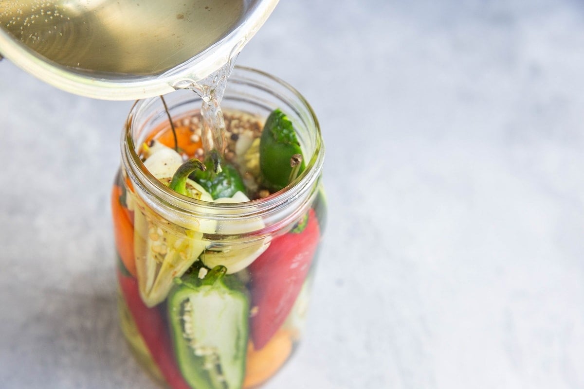 Pouring pickling brine into the jar with the peppers.