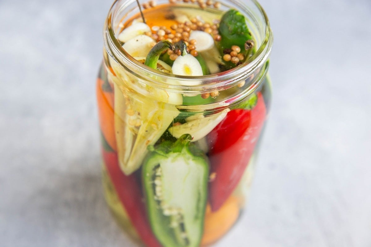 Jar of peppers in liquid, ready to be sealed for pickled peppers.