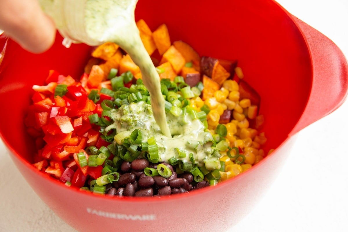 Pouring dressing into a large bowl with salad ingredients.