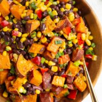 Wooden bowl of roasted sweet potato salad with a gold spoon to serve.