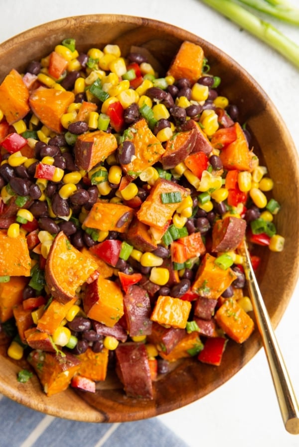 Wooden bowl of roasted sweet potato salad with a gold spoon to serve.