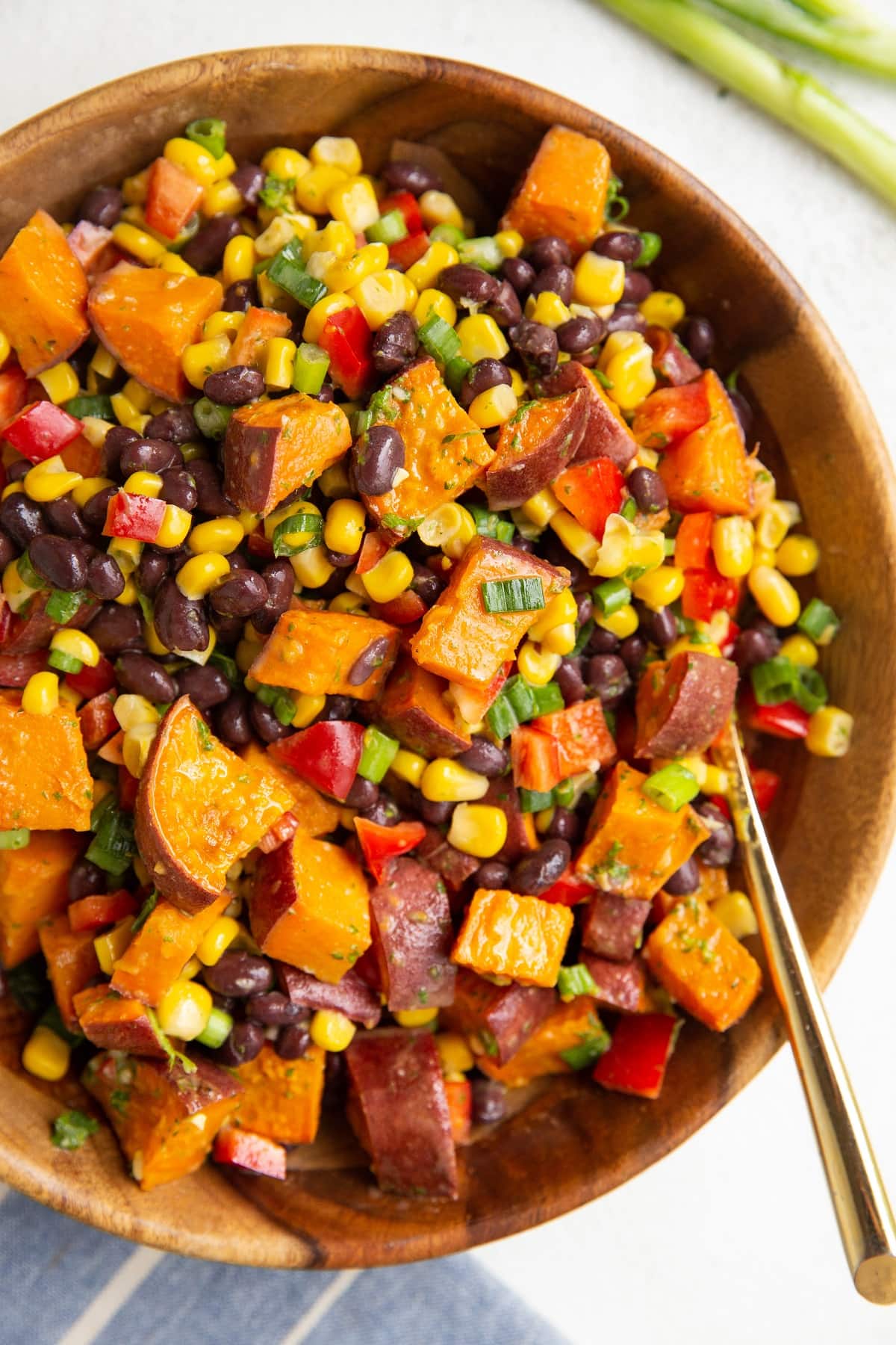 Wooden bowl of roasted sweet potato salad with a gold spoon to serve.