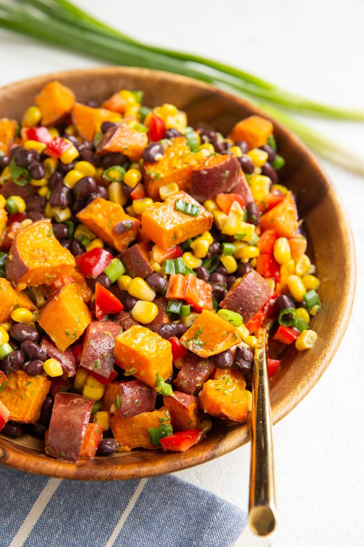 Wooden bowl full of sweet potato black bean salad with a blue napkin to the side and a gold serving spoon.