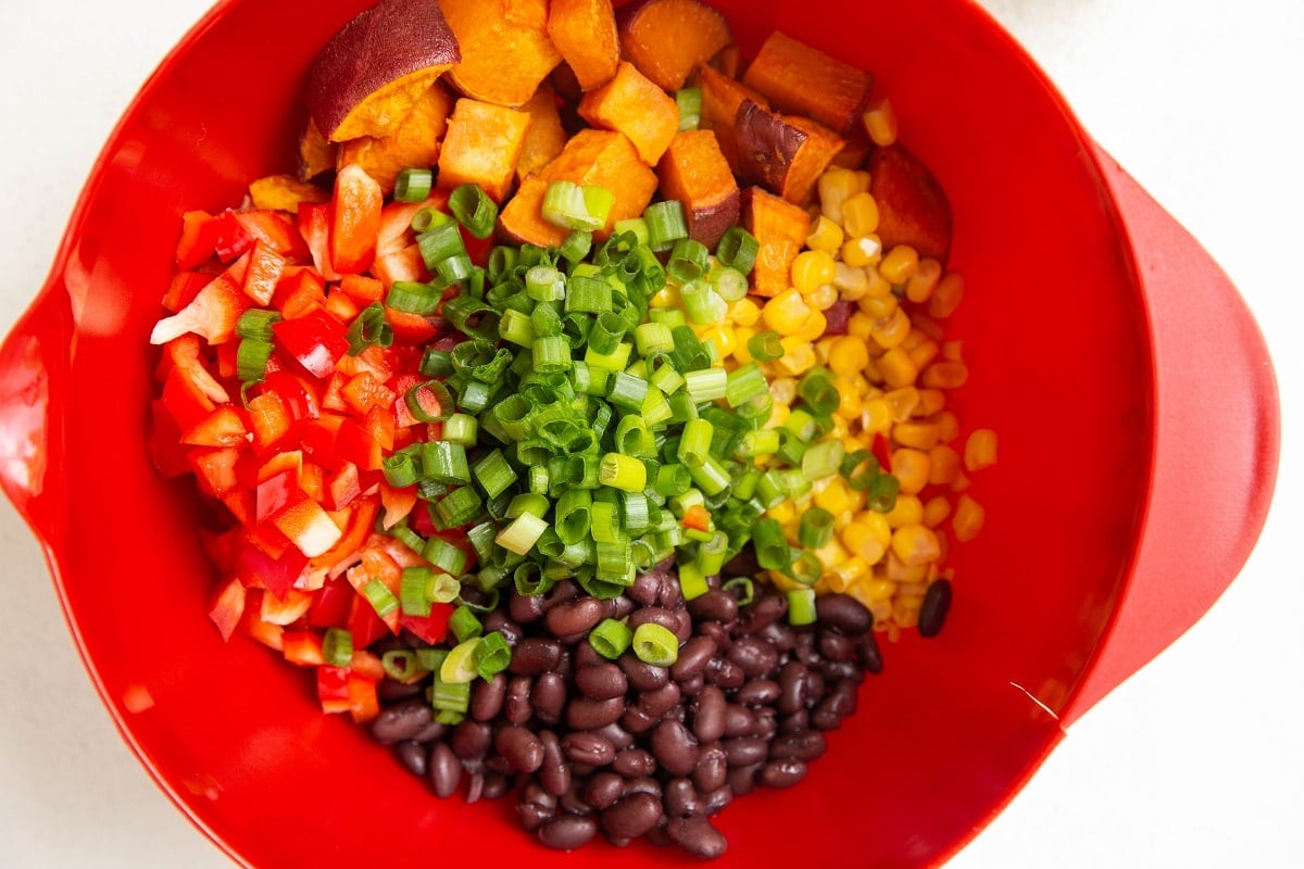 Ingredients for sweet potato black bean salad in a red mixing bowl.