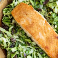 Big wooden bowl of green goddess salad with crispy salmon on top.