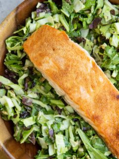 Big wooden bowl of green goddess salad with crispy salmon on top.