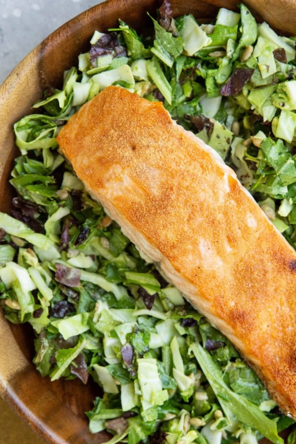 Big wooden bowl of green goddess salad with crispy salmon on top.