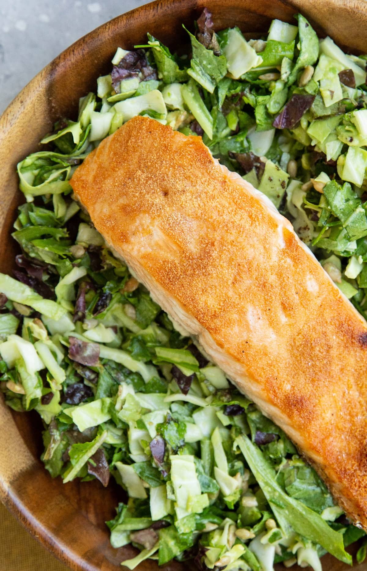 Big wooden bowl of green goddess salad with crispy salmon on top.