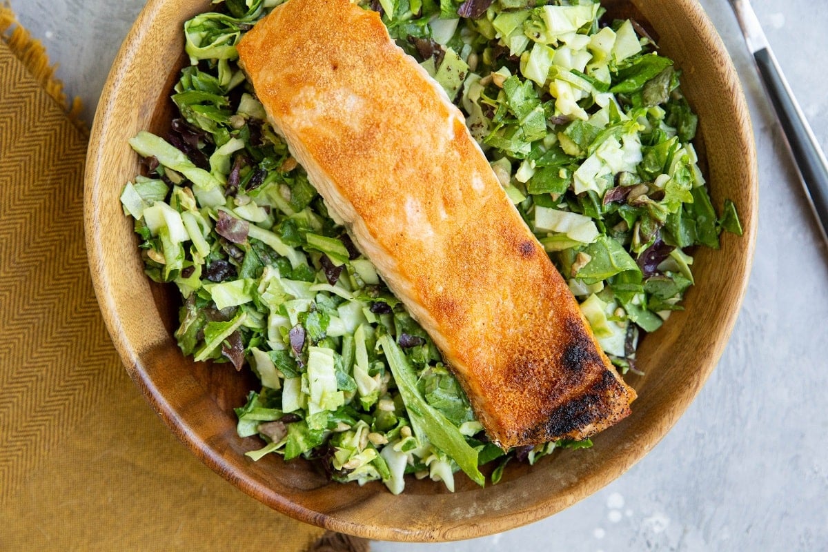 Wooden bowl of salad with cooked salmon on top