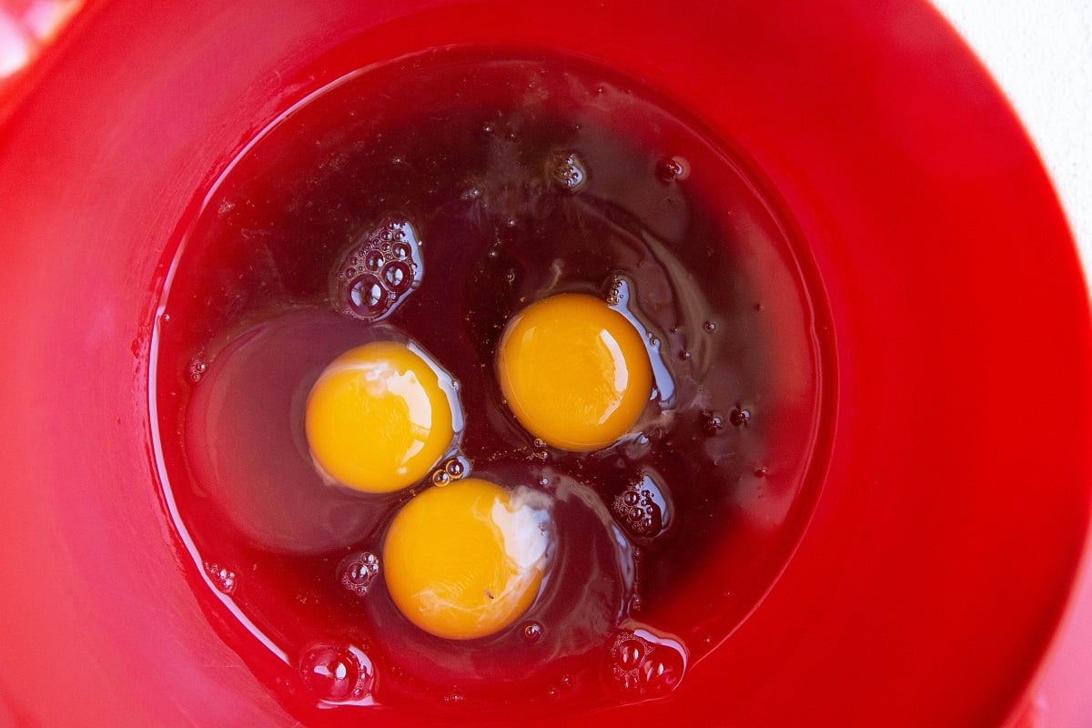 Eggs, pure maple syrup and vanilla extract in a red mixing bowl.