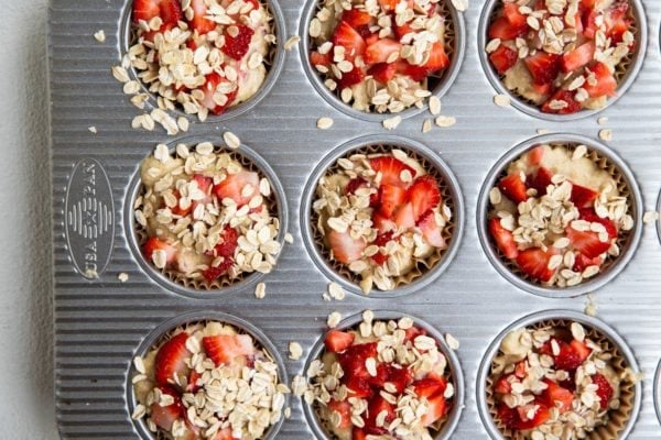 Strawberry muffin batter in a muffin tray with oatmeal and strawberries sprinkled on top.