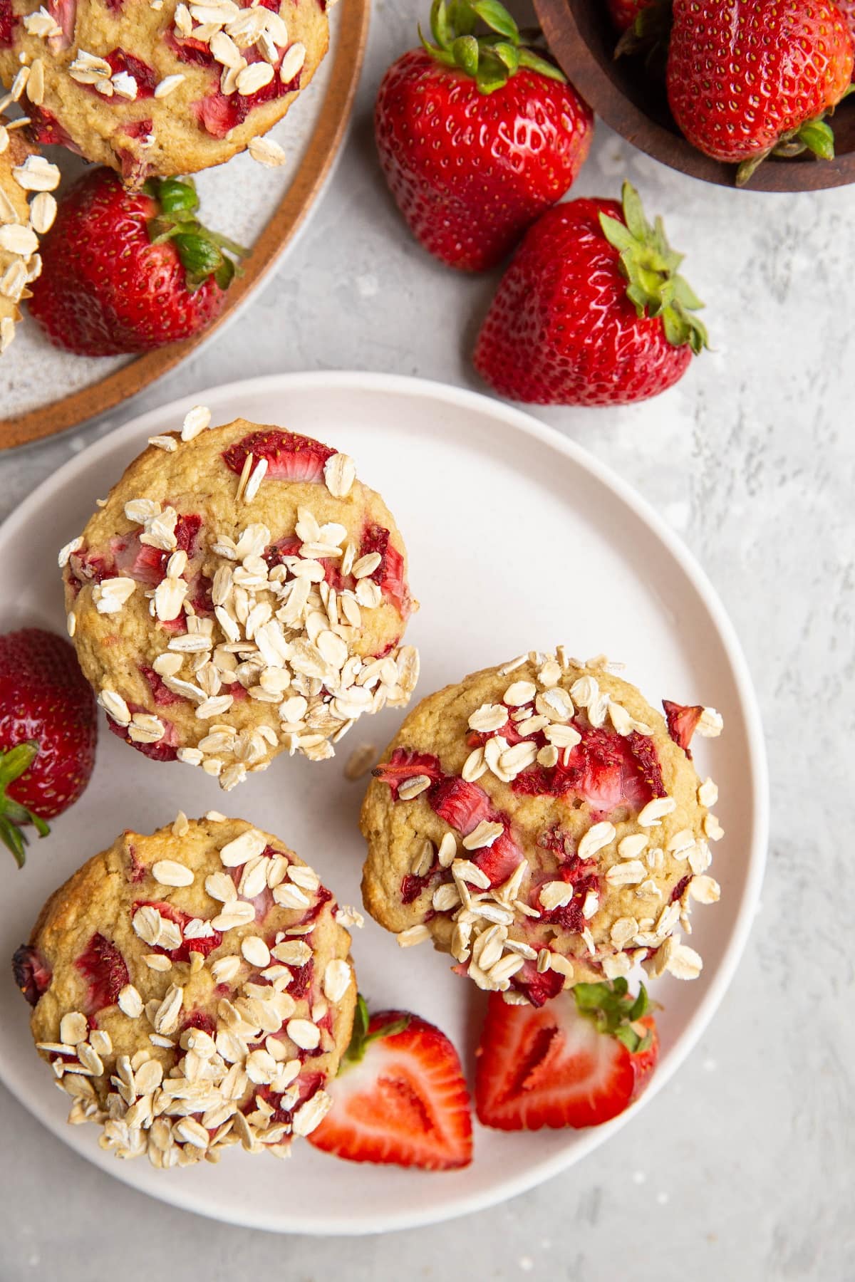 Two plates with strawberry muffins and fresh strawberries to the side.