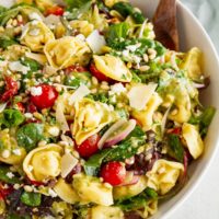 Tortellini Salad in a large white bowl with salad tongs ready to serve.