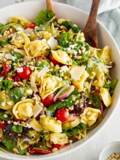 Tortellini Salad in a large white bowl with salad tongs ready to serve.