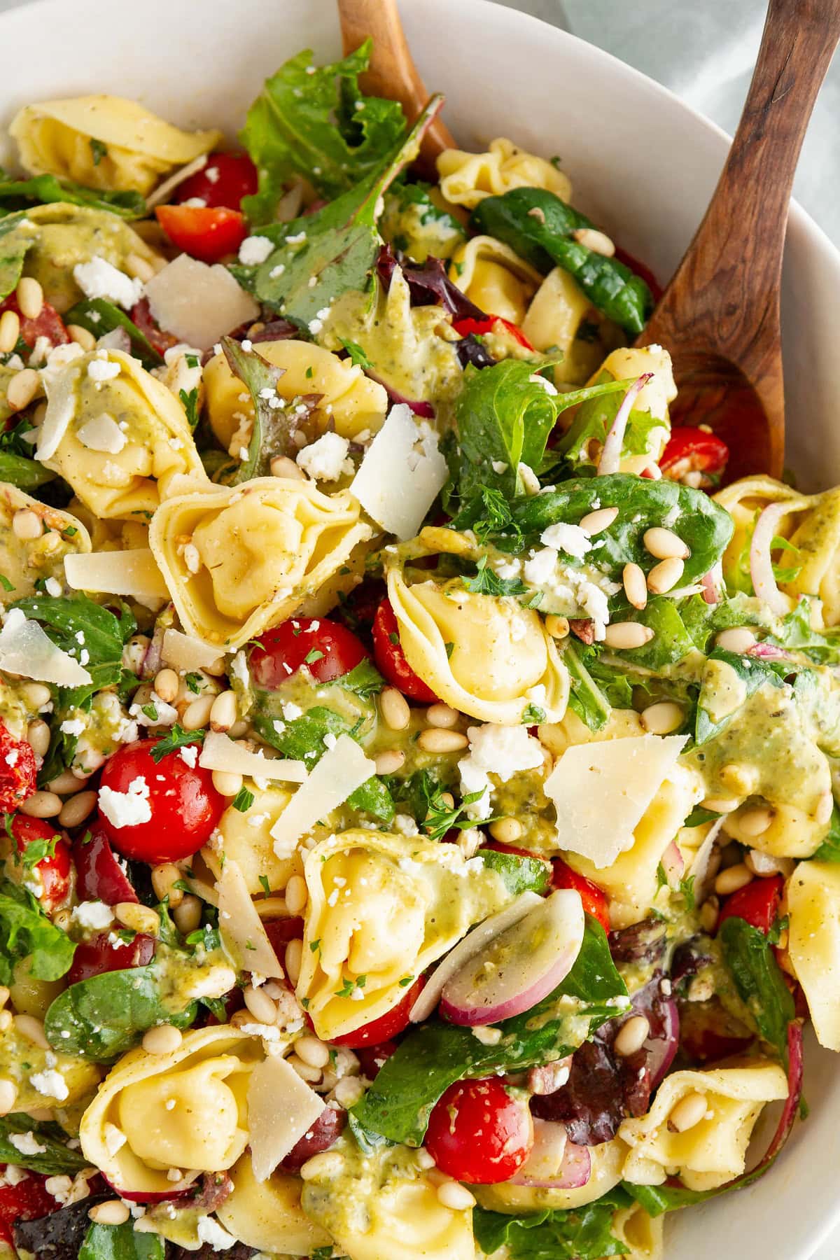 Large white serving bowl of pasta salad with wooden serving spoons.