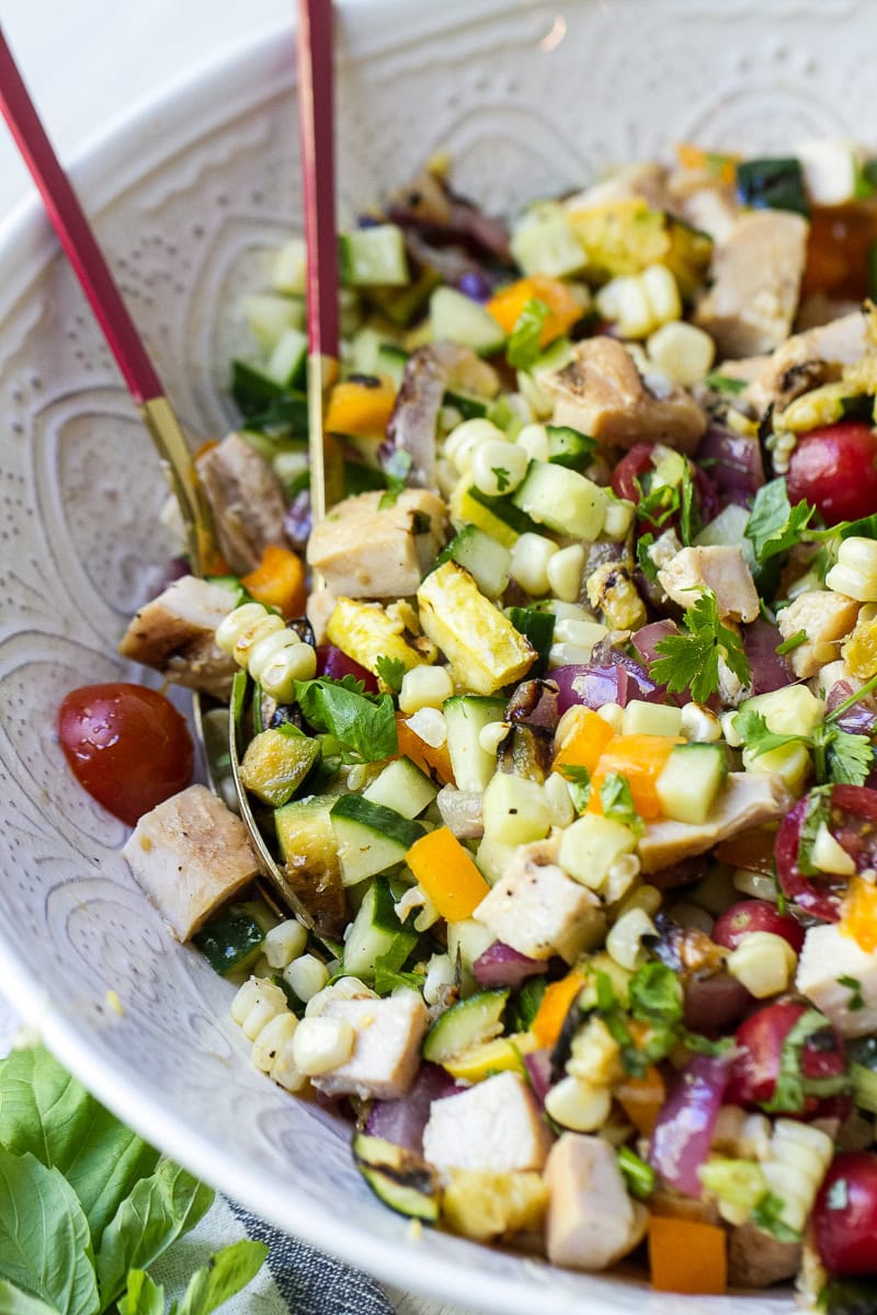 Rotisserie Chicken and Grilled Vegetable Salad in a bowl wit serving spoons.