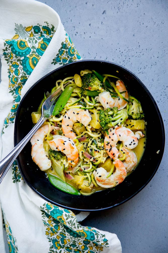 Black bowl of Thai Green Curry Zoodles with Shrimp and Broccoli with a napkin to the side.