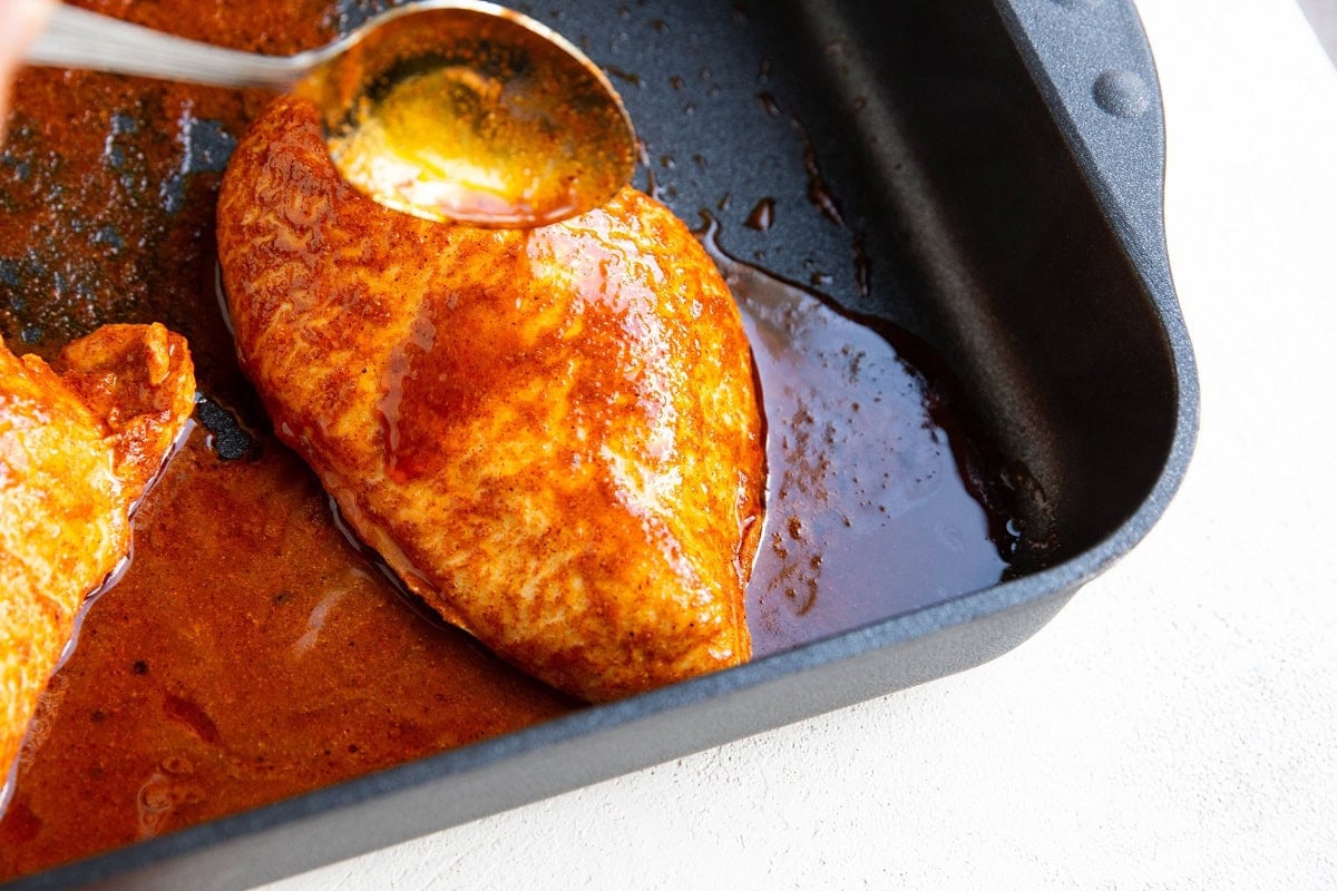 A spoon pouring juices over the chicken.