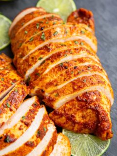 Two large chicken breasts on a black cutting board, cut into slices.