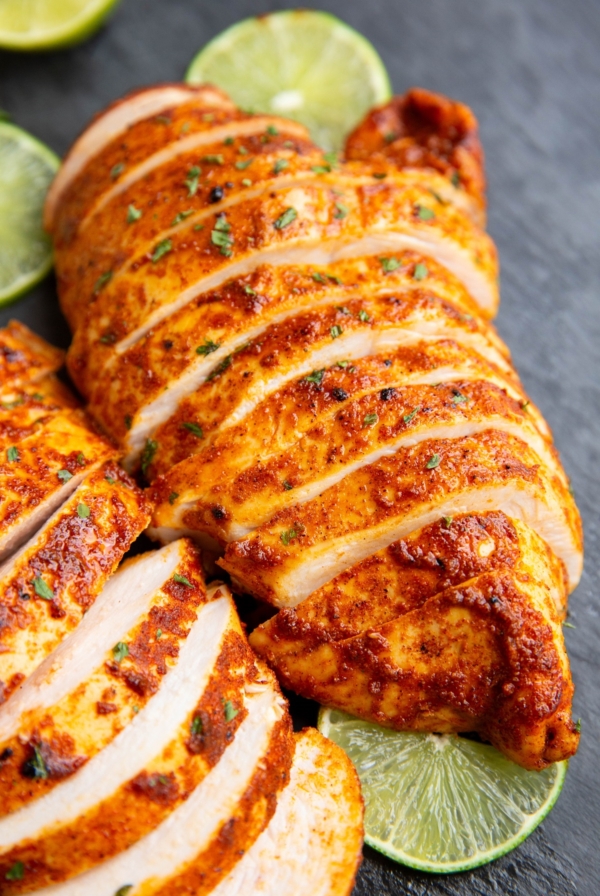 Two large chicken breasts on a black cutting board, cut into slices.
