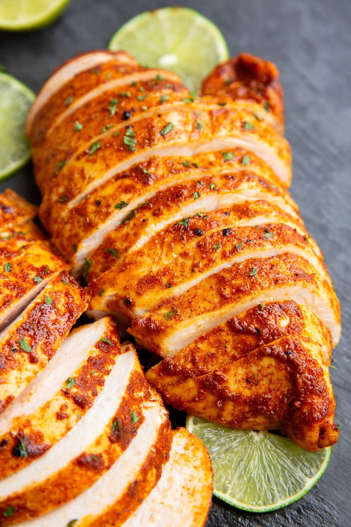 Two large chicken breasts on a black cutting board, cut into slices.