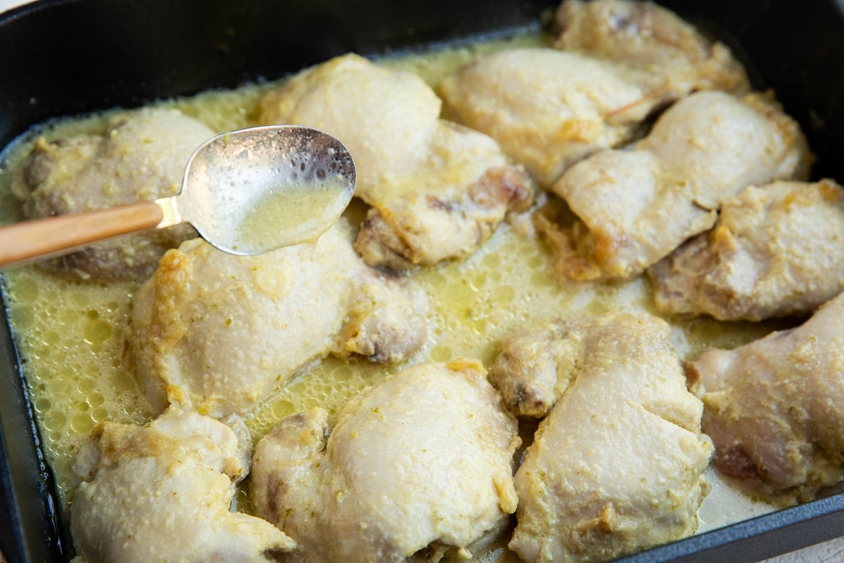 Spoon pouring juices over baked chicken thighs.
