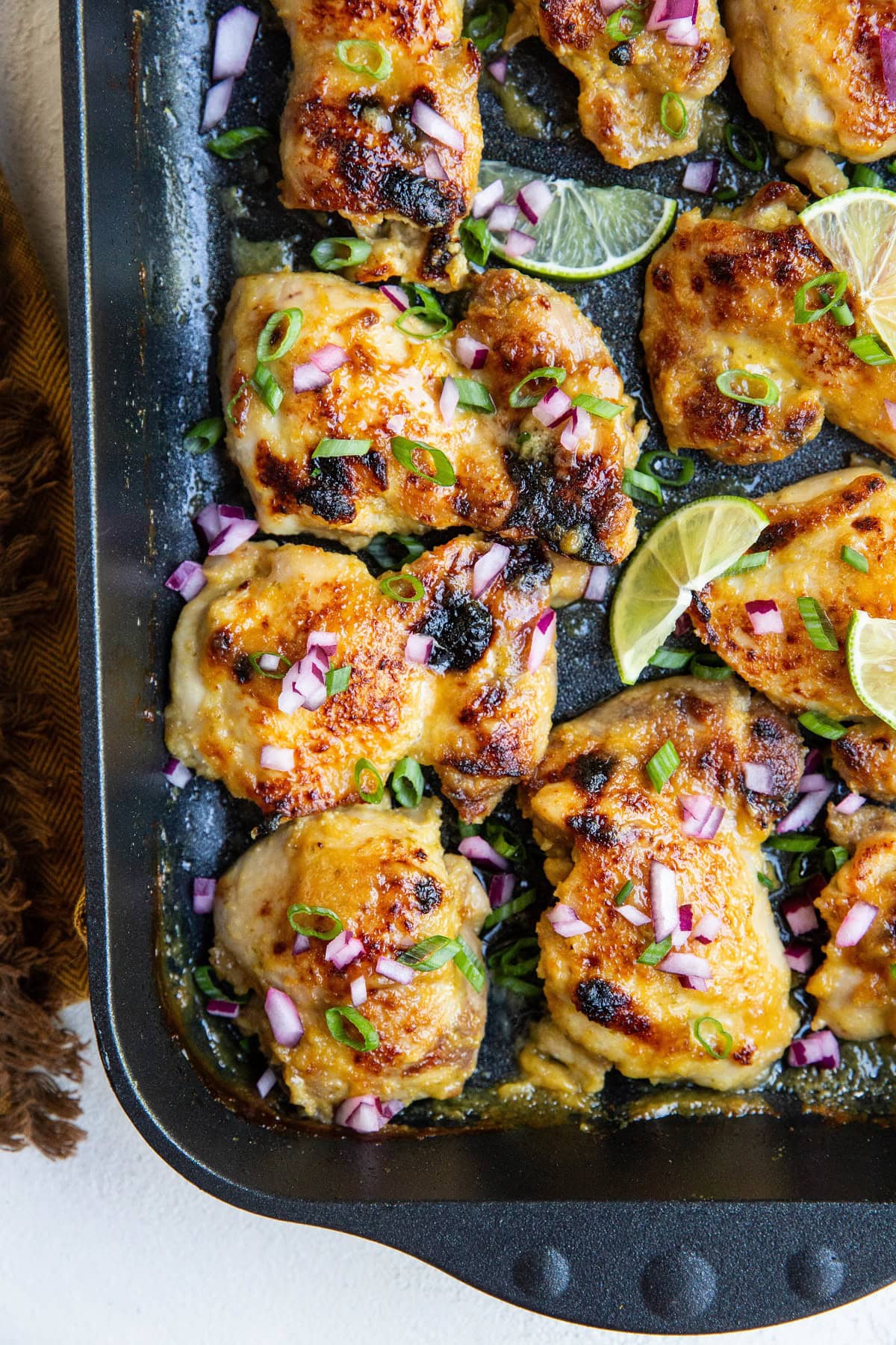 Black roasting pan of Cuban chicken sprinkled with onions and lime slices.