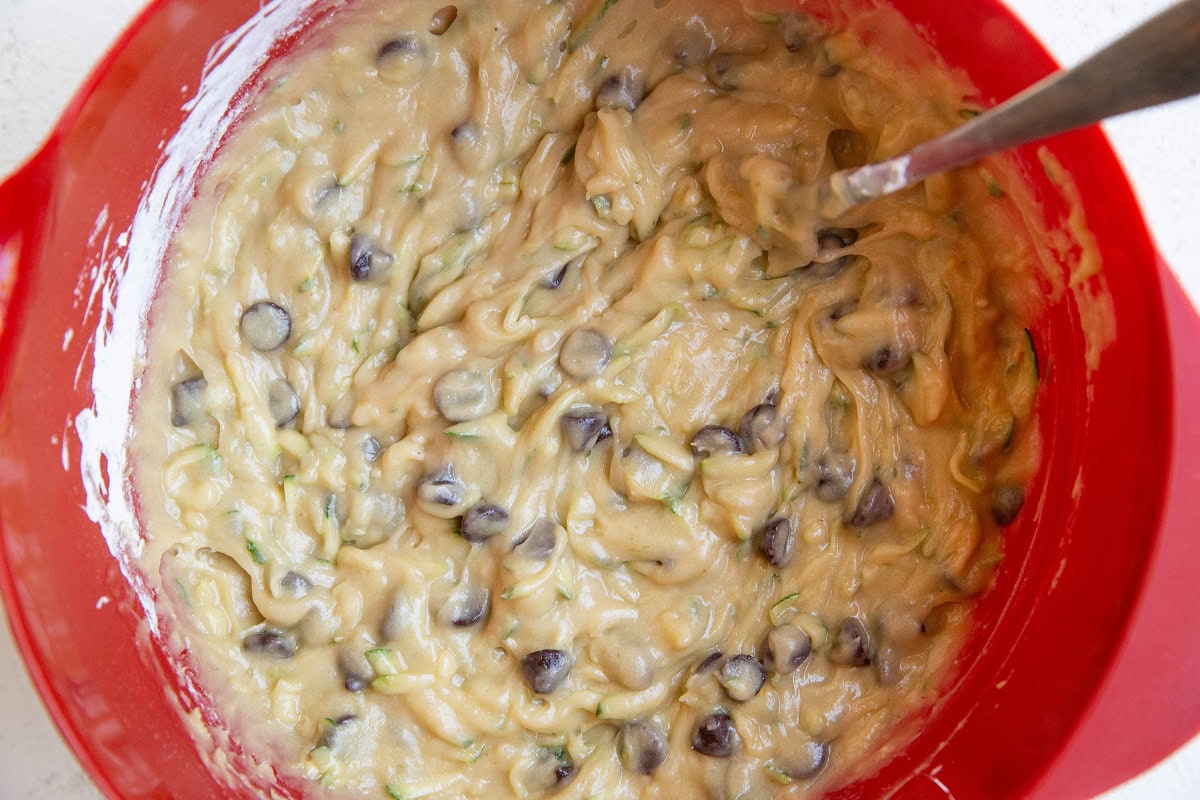 Zucchini bread batter in a red mixing bowl with chocolate chips.