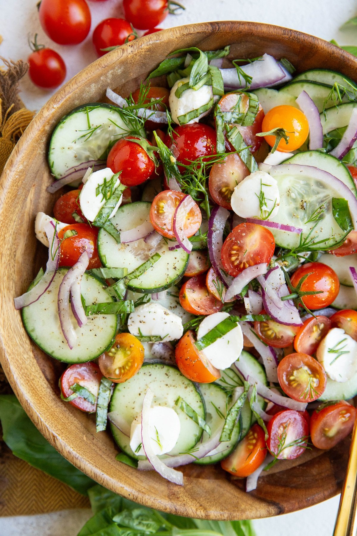 Cucumber tomato salad in a wooden bowl with red onion, mozzarella cheese and fresh herbs.