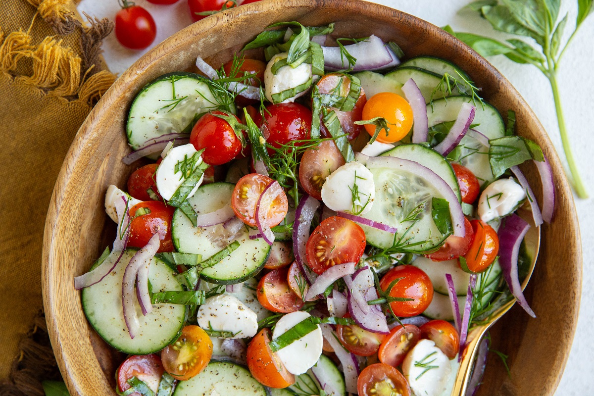 Wooden bowl full of fresh vegetables for cucumber tomato salad.