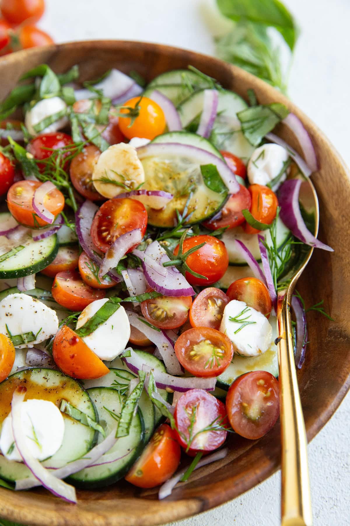 Cucumber tomato salad with balsamic vinegar drizzled on top with a gold spoon.