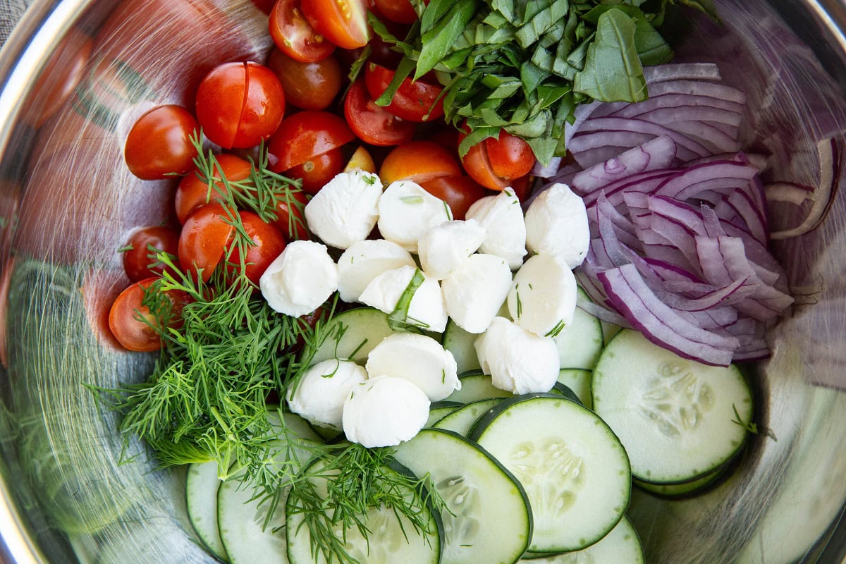 Ingredients for cucumber tomato salad in a stainless steel mixing bowl, ready to be mixed.