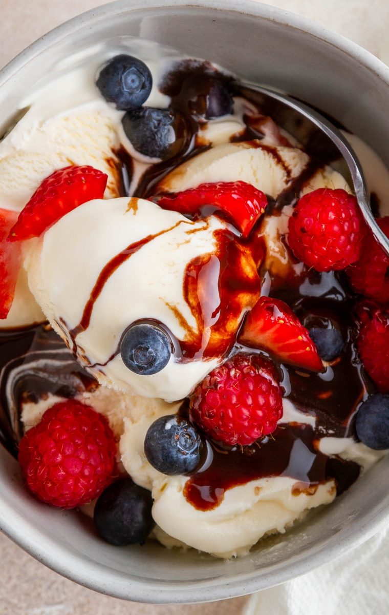 Close up image of vanilla ice cream with fresh berries and chocolate sauce, ready to eat.