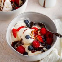 Two bowls of vanilla ice cream with fresh berries and chocolate sauce, ready to serve.