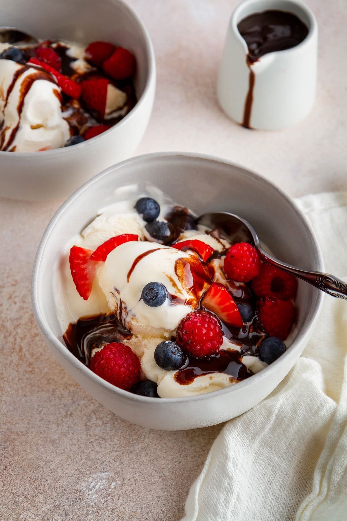 Two bowls of vanilla ice cream with fresh berries and chocolate sauce, ready to serve.