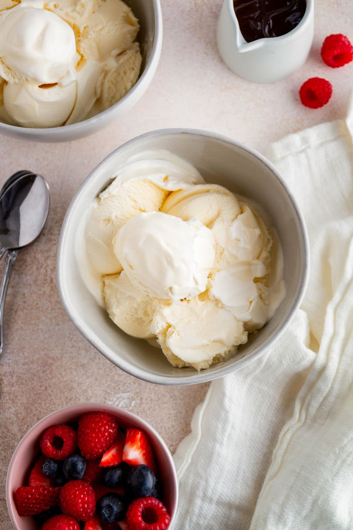 Two bowls of vanilla ice cream with a bowl of fresh berries to the side and a container of chocolate sauce, ready to eat.