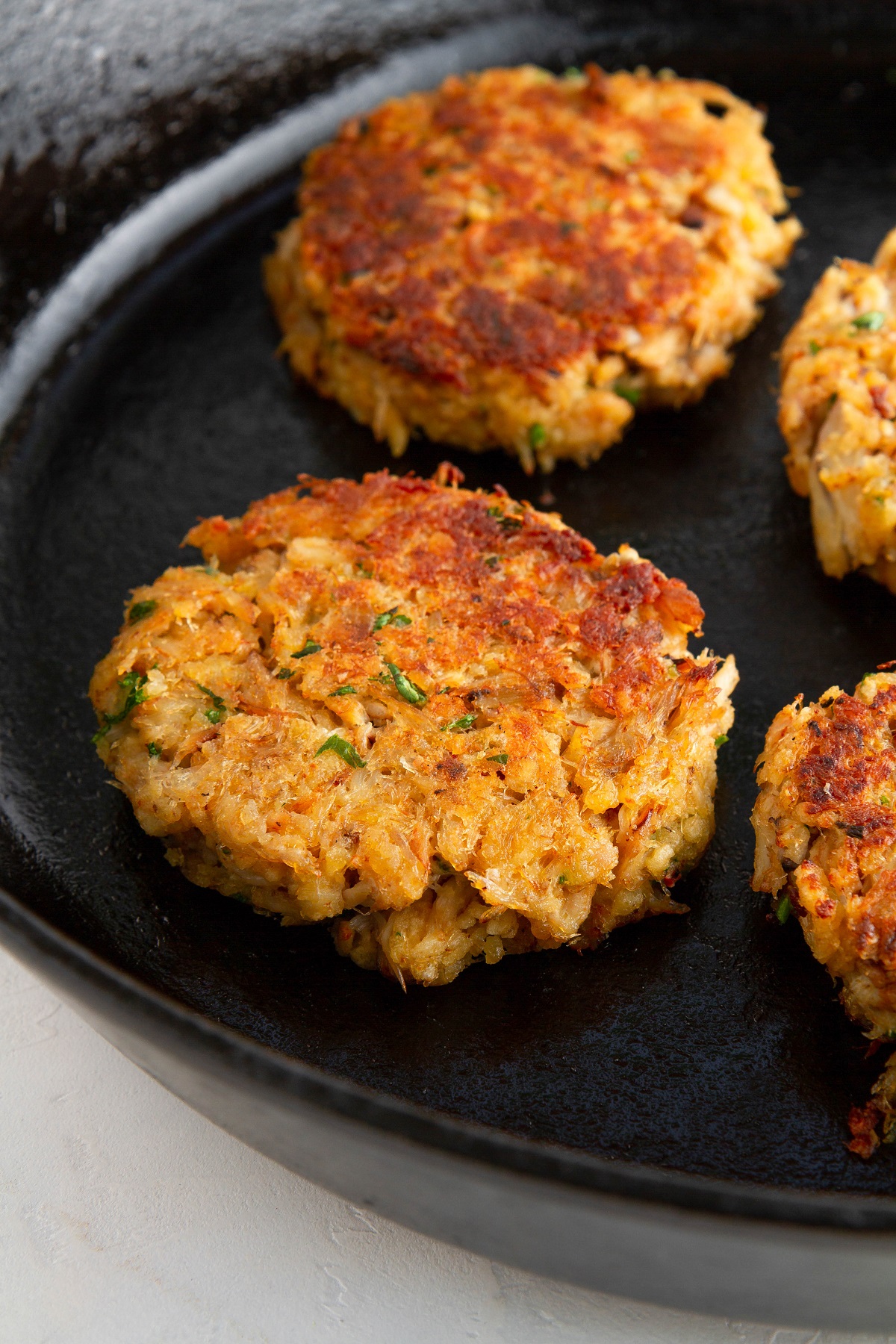 Crab cakes cooking in a cast iron skillet to golden brown perfection.