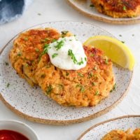 Three appetizer plates of crab cakes with tartar sauce, cocktail sauce, and lemon wedges.