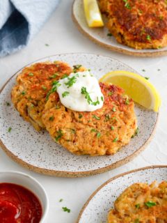 Three appetizer plates of crab cakes with tartar sauce, cocktail sauce, and lemon wedges.