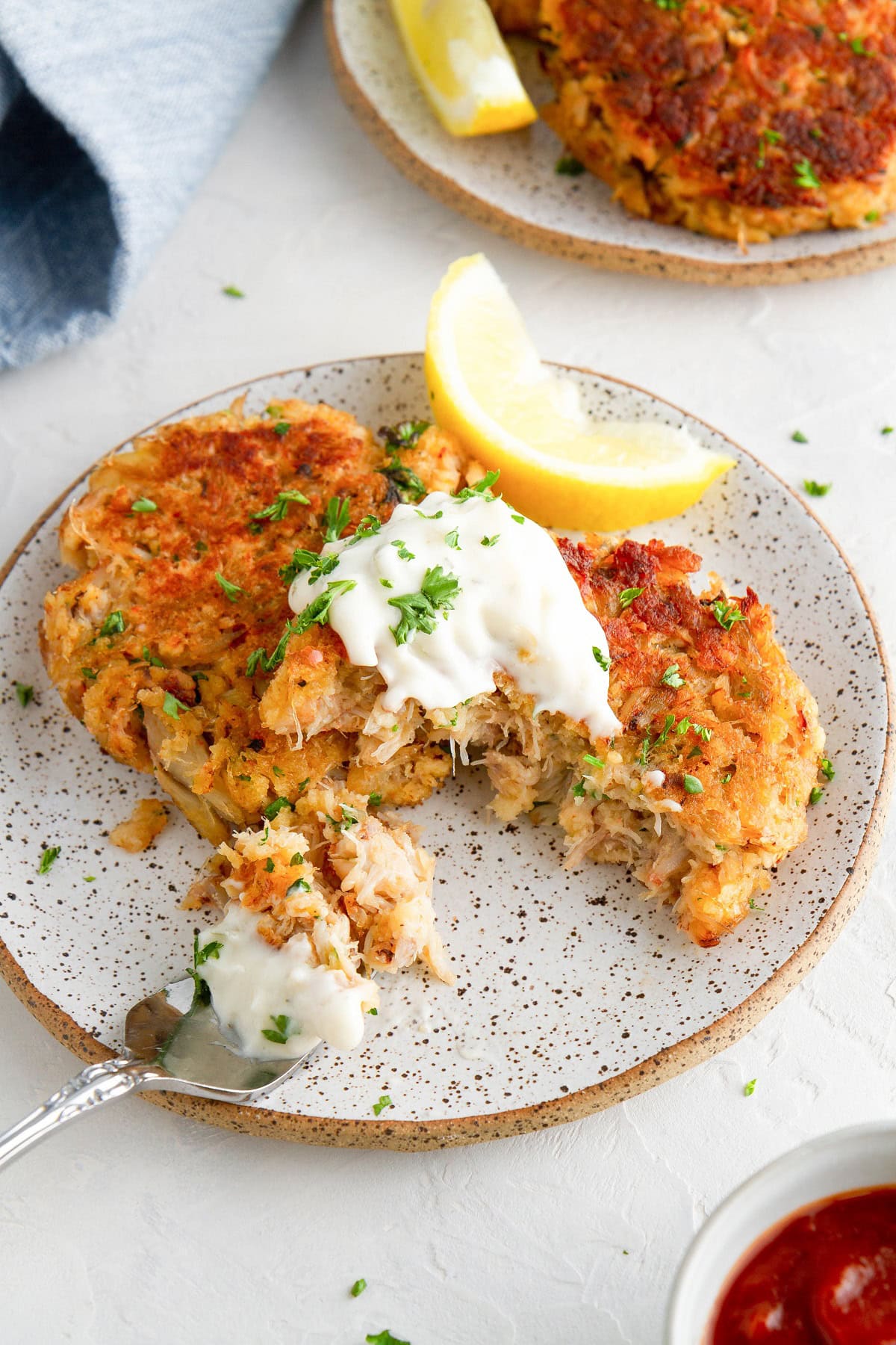 Crab cakes on a plate with a fork taking a bite out of one of them.