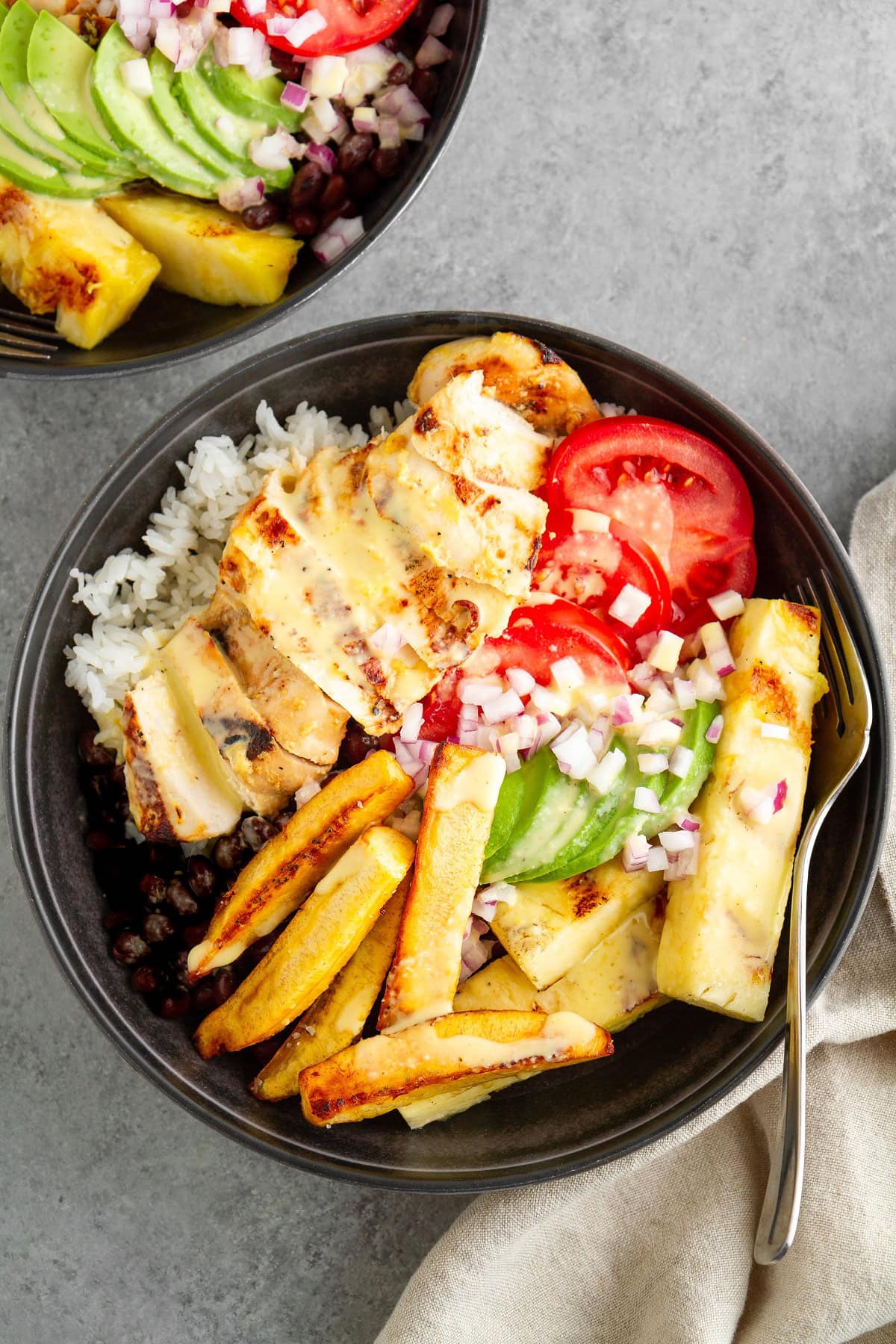 Black bowls full of rice, beans, mojo chicken, fried plantains, avocado and tomatoes