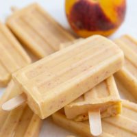 Creamy healthy peach popsicles on a white background and a fresh peach.