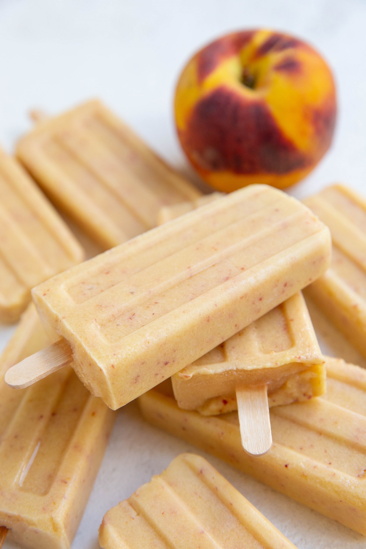Creamy healthy peach popsicles on a white background and a fresh peach.