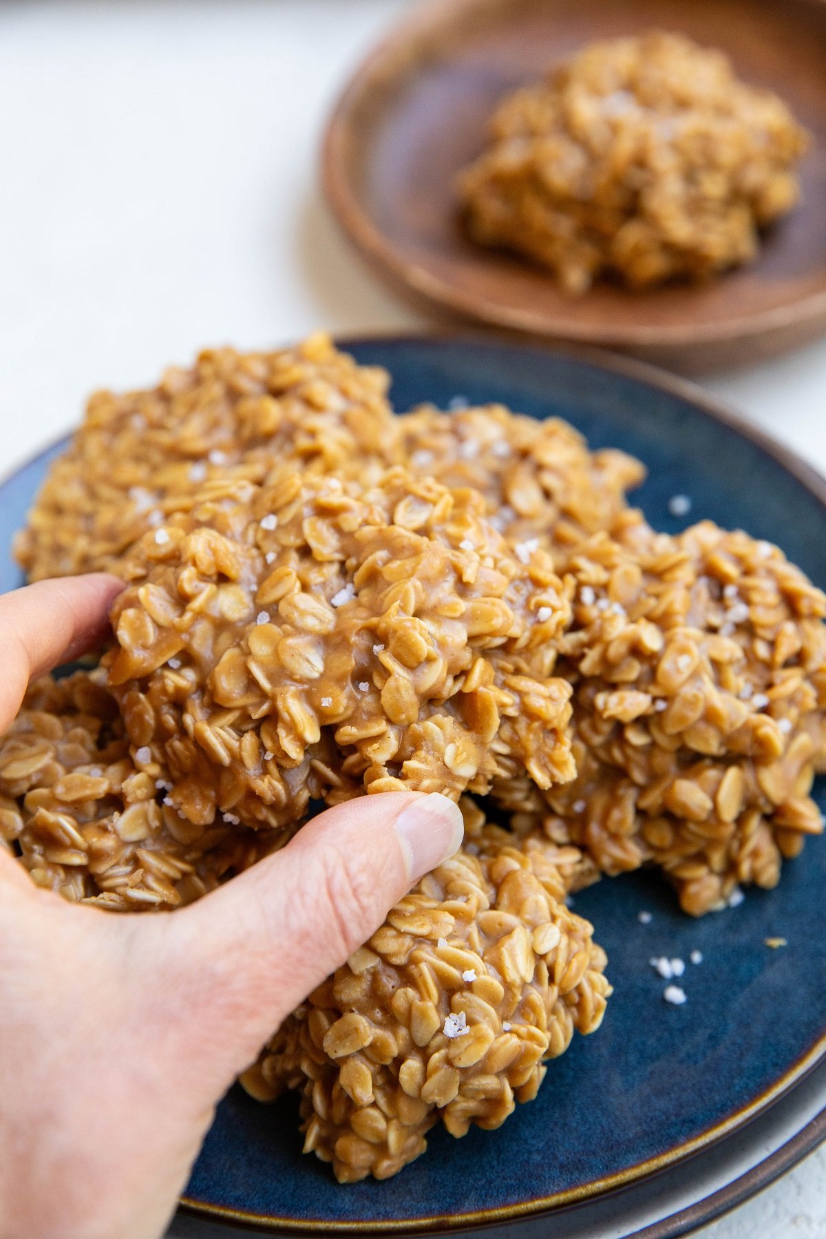 Hand grabbing a peanut butter oatmeal cookie off of a plate.